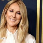 Celine Dion smiling on stage announcing her Paris comeback concert after Stiff Person Syndrome