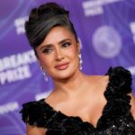 Salma Hayek showcasing her natural gray hair in a sheer black Gucci gown on the red carpet at the Breakthrough Prize ceremony